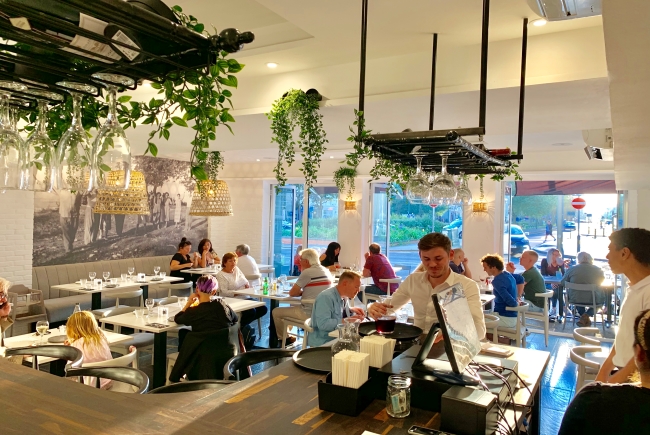 Nostos restaurant during a busy lunchtime service, image show plats and wine glasses with a busy restaurant int he background.